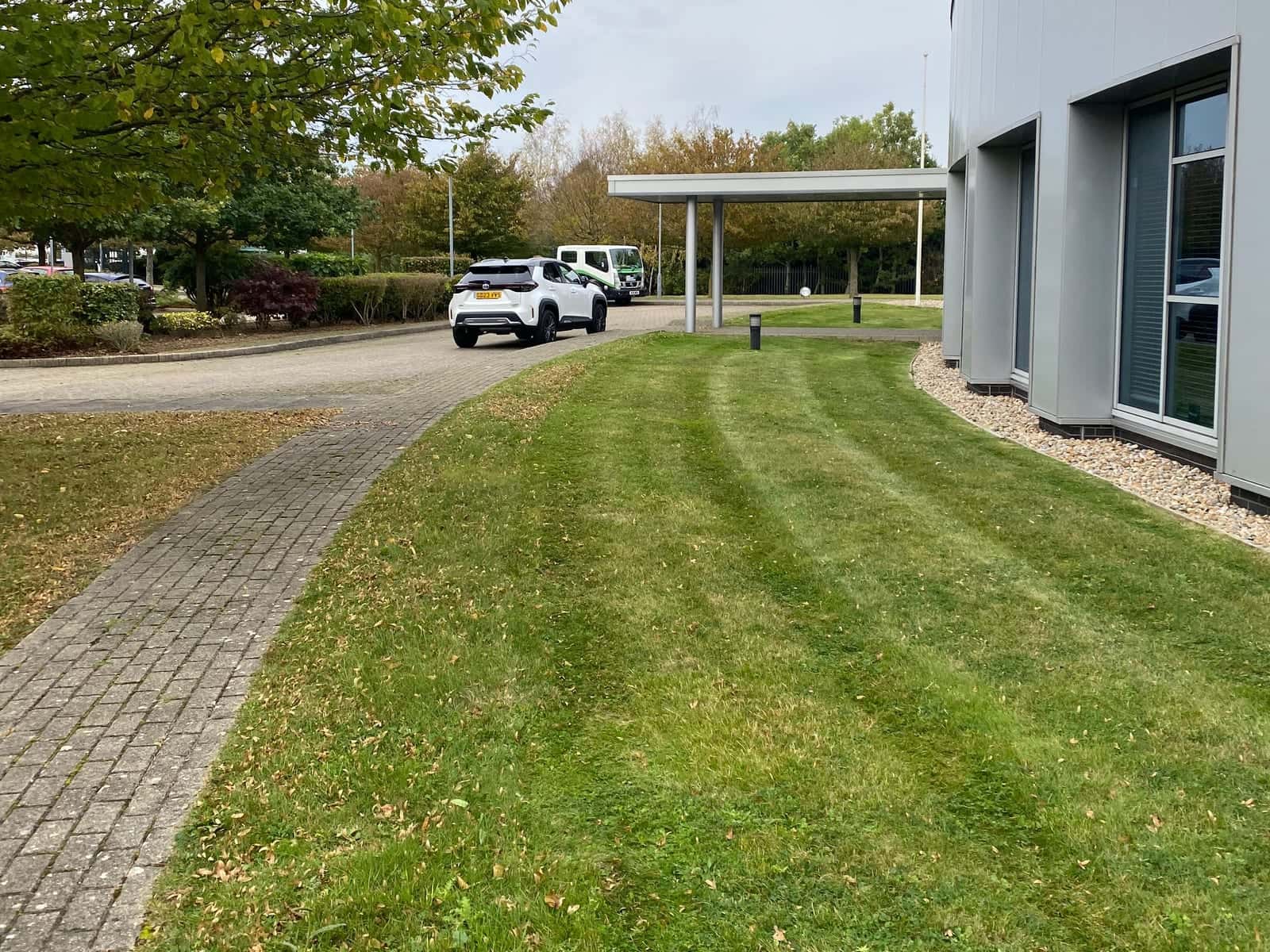 Neatly striped grass following the curve of a modern commercial building beside a block-paved path