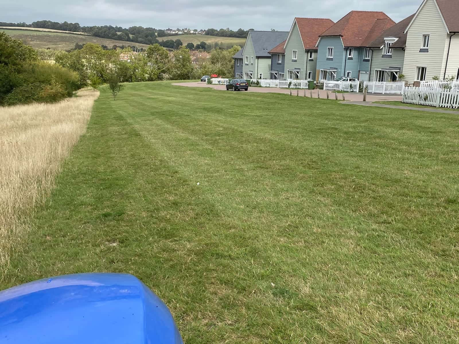 Mowing stripes across open grass beside a row of new houses, seen from a ride-on mower