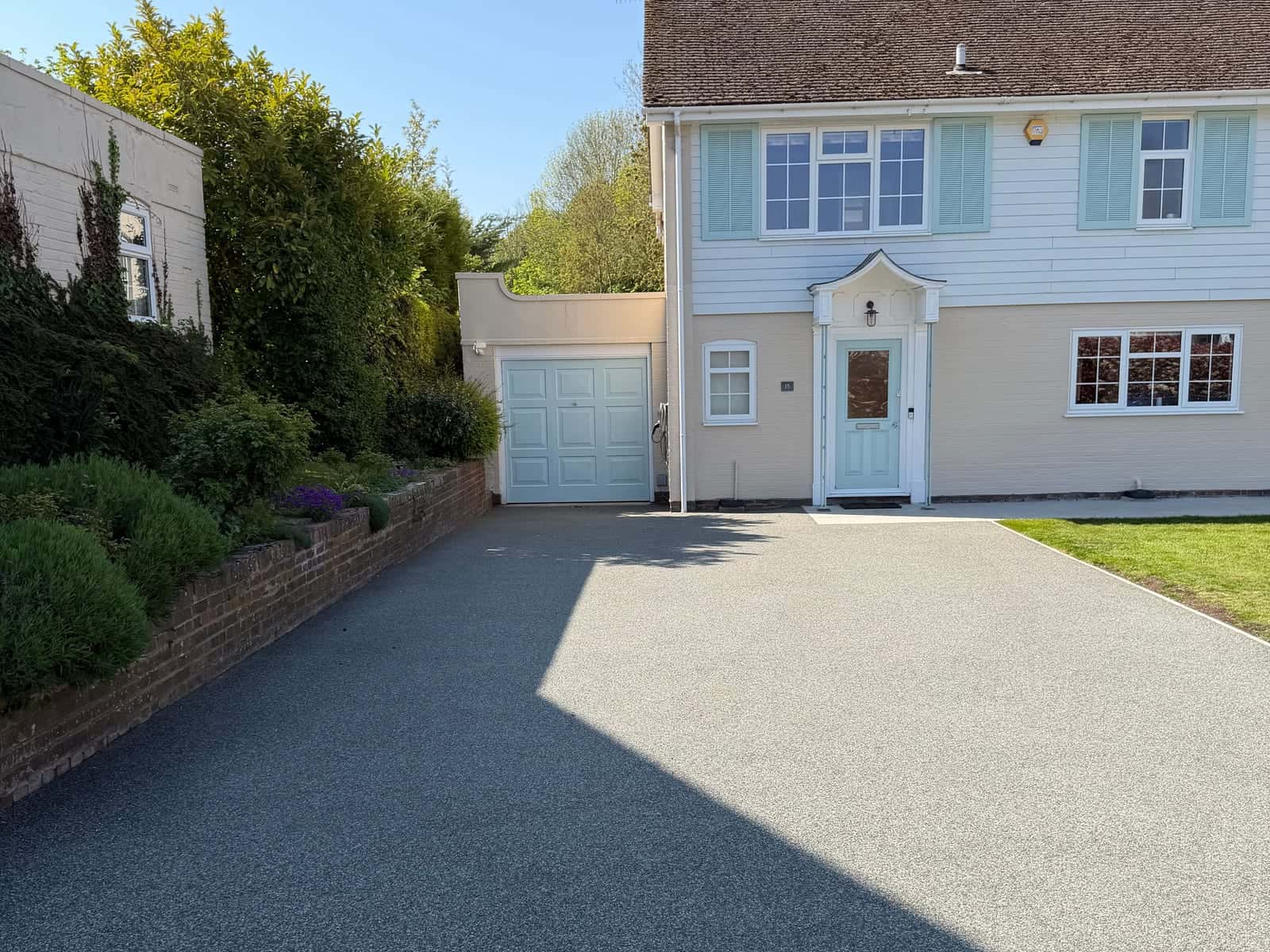 A new speckled grey driveway surface in front of a house with a garage, edged with a slate border