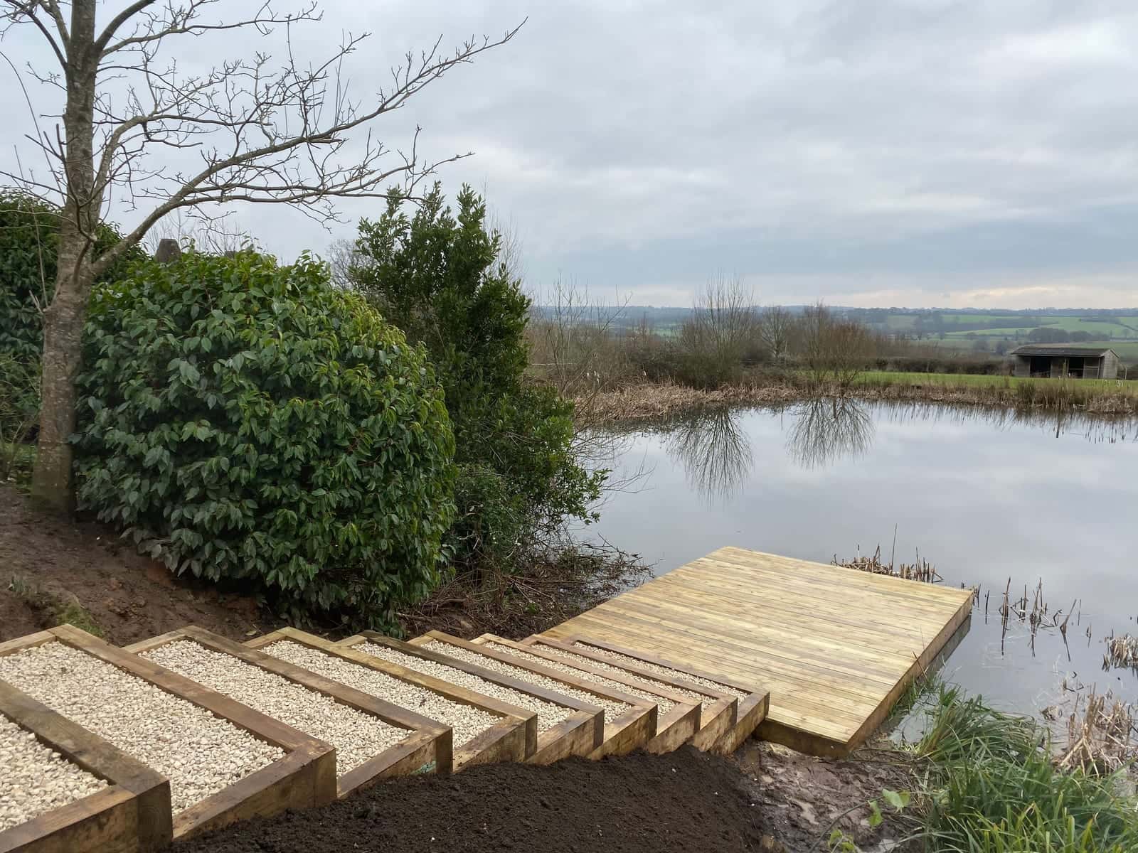 Gravel-filled sleeper steps leading down a bank to a timber jetty on a lake