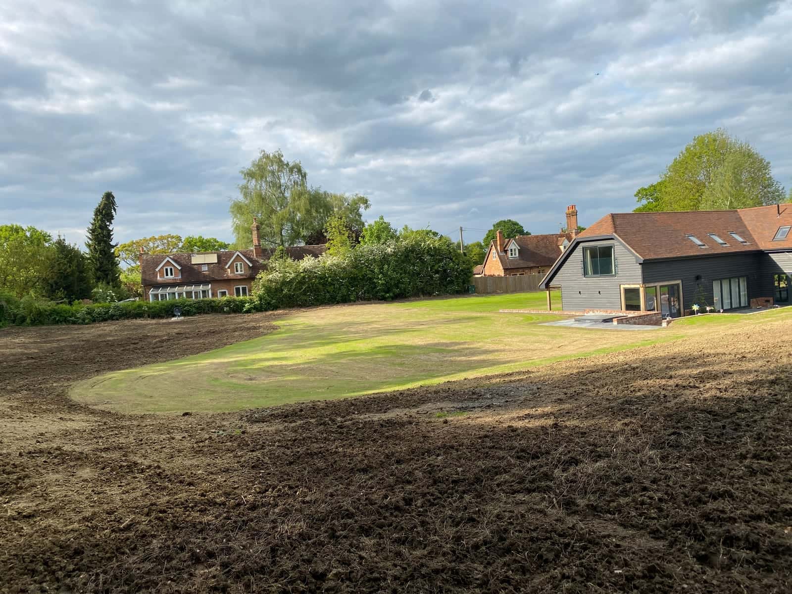 A large garden graded and sown, with new grass coming through around a timber-clad house