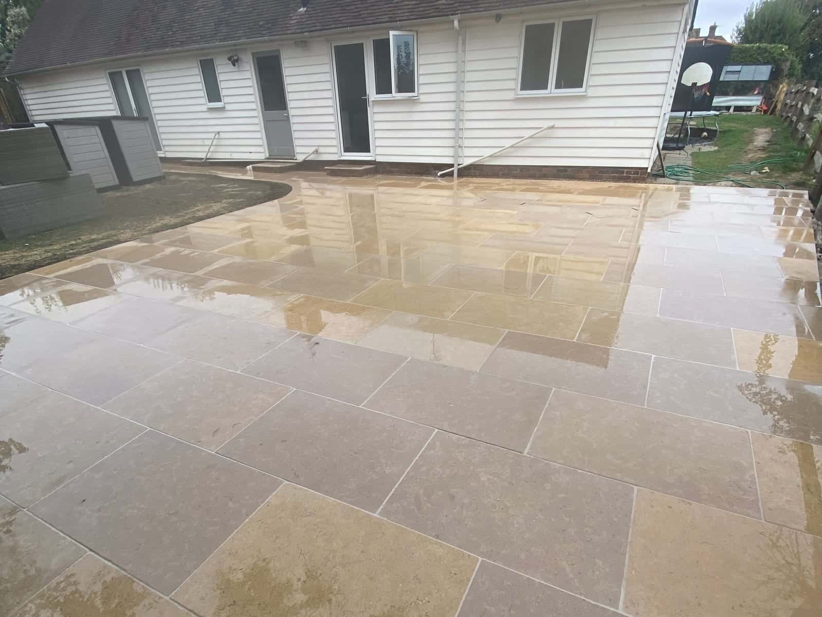 A large natural stone patio, wet from rain, laid across the back of a white weatherboarded bungalow