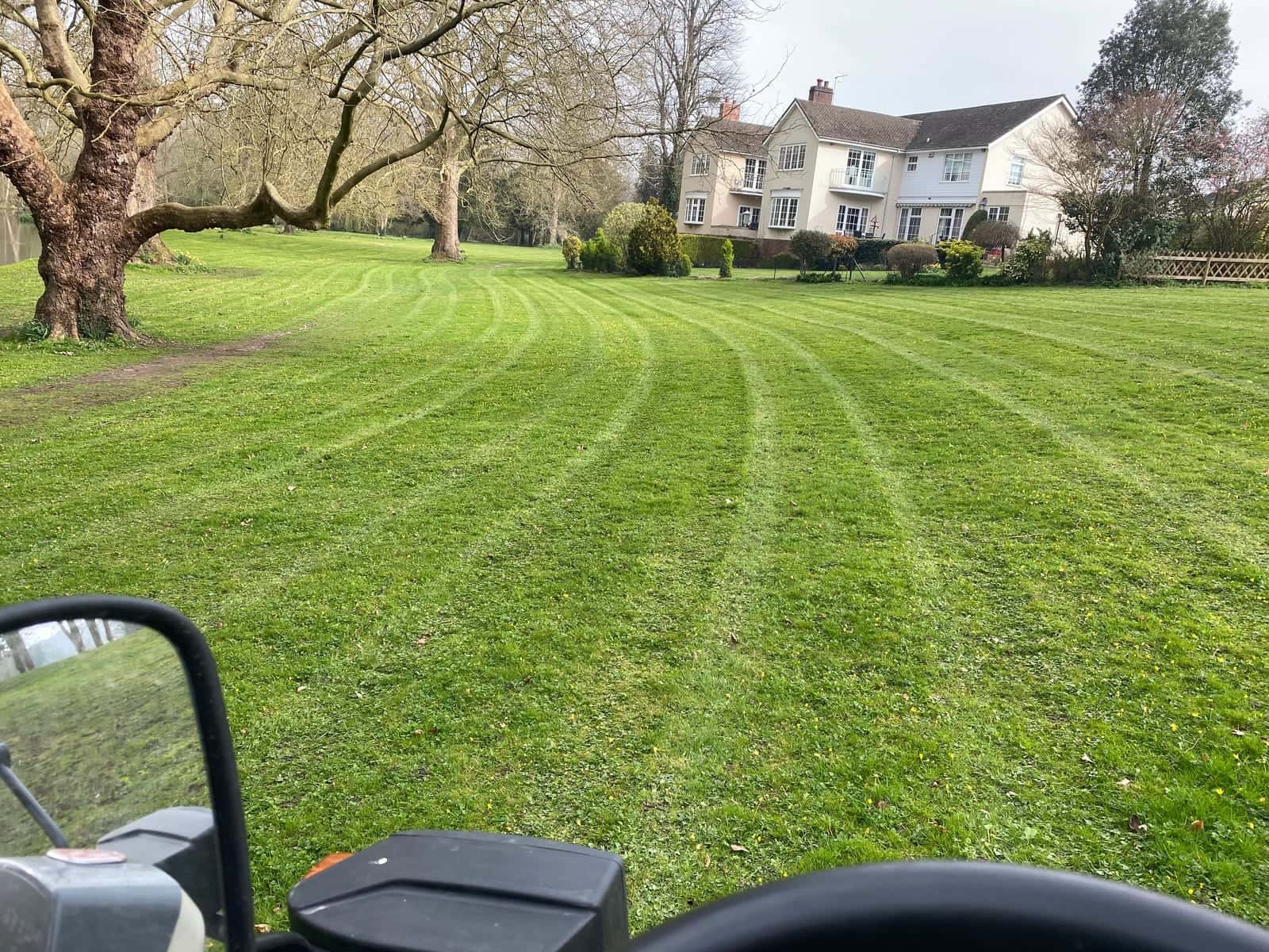 Fresh mowing stripes curving across a large lawn towards a substantial house, seen from the mower seat