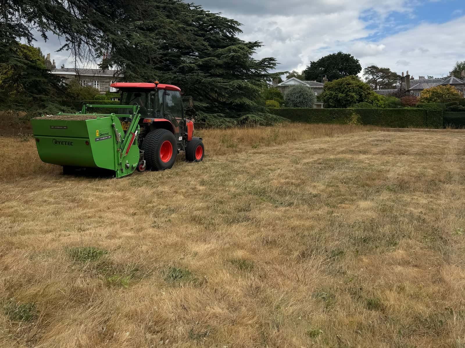 A tractor with a flail collector cutting long, dry grass across an open field