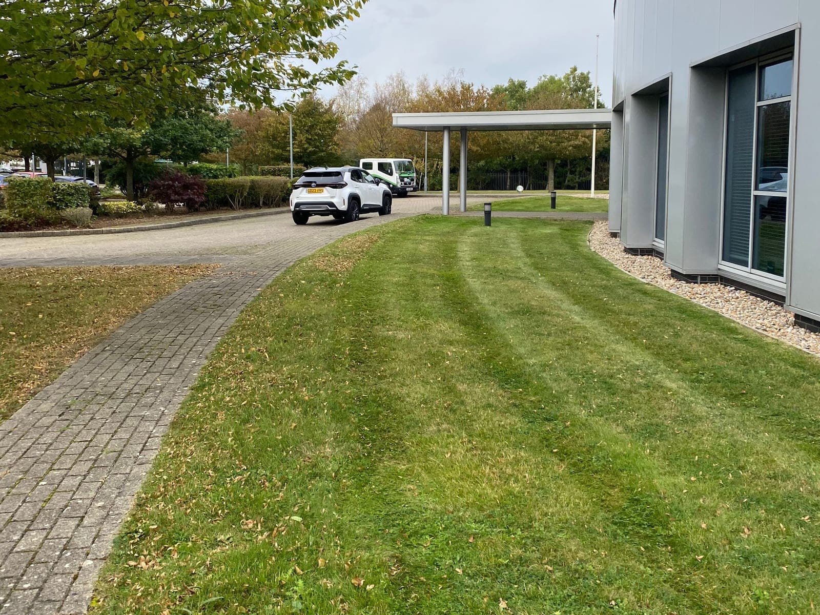 Neatly striped grass following the curve of a modern commercial building beside a block-paved path