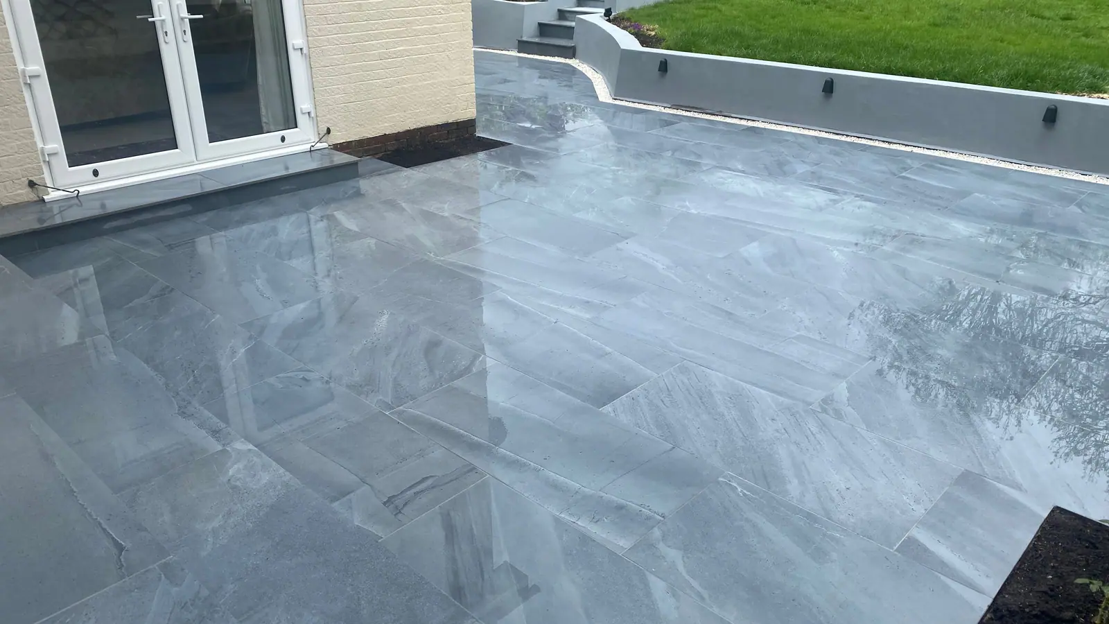 The finished grey paved terrace outside French doors, with a rendered wall and steps up to the lawn