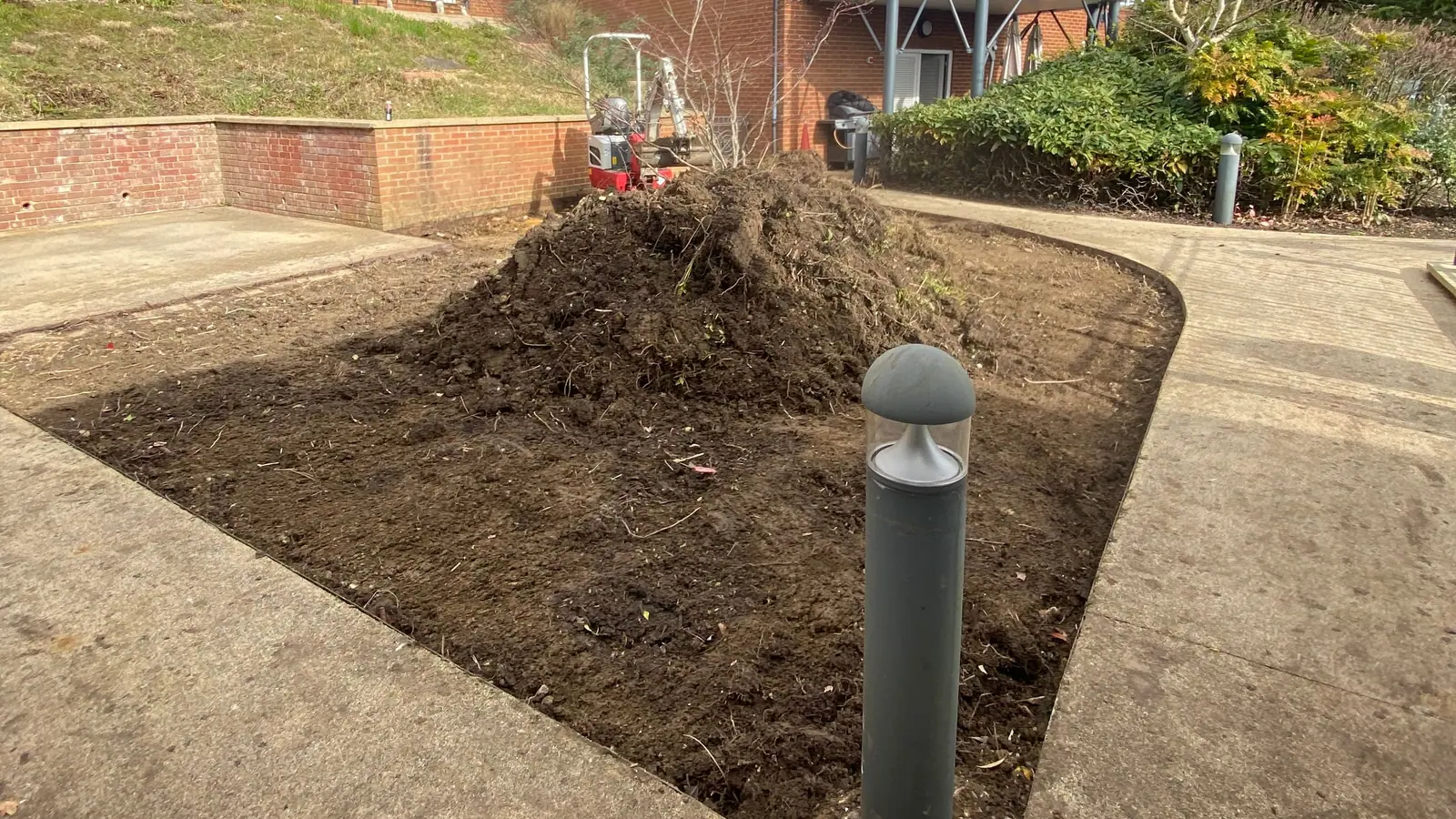 The courtyard bed cleared to bare soil around a lamp bollard, with a heap of spoil in the middle